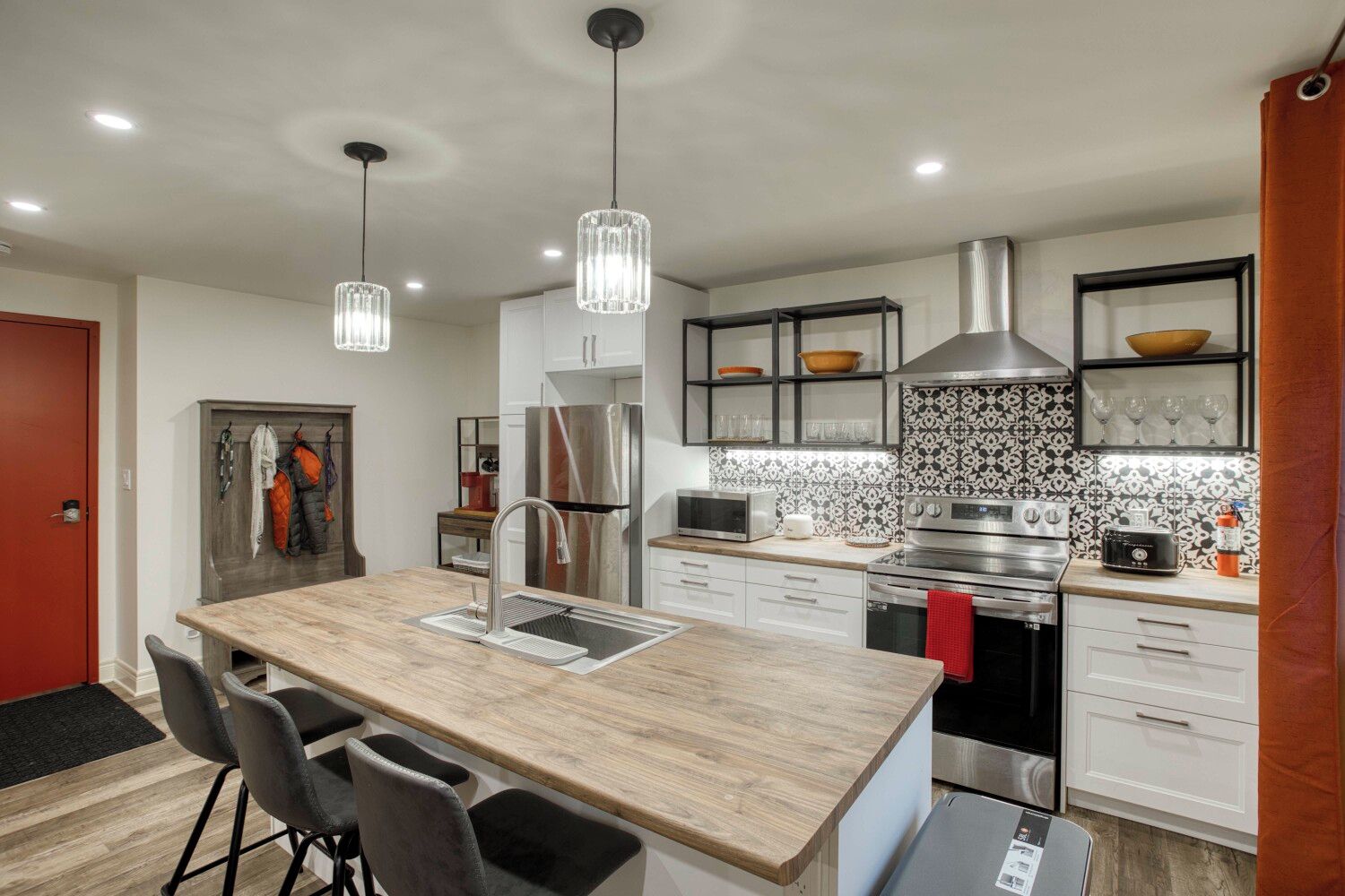 A modern kitchen with a central island, stainless steel appliances, pendant lighting, and a patterned backsplash.