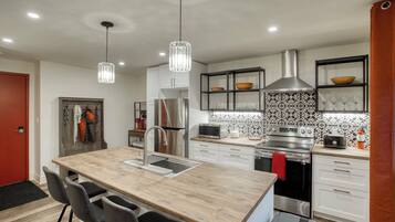 A modern kitchen with a central island, stainless steel appliances, pendant lighting, and a patterned backsplash.