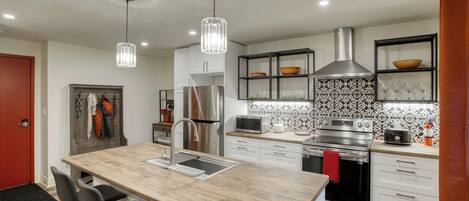 A modern kitchen with a central island, stainless steel appliances, pendant lighting, and a patterned backsplash.