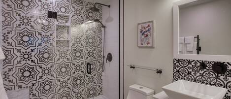 Un baño con pared de ducha con diseño, un inodoro, un lavabo y un espejo.