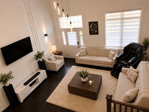 En stue med et fladskærms-tv, en beige sofa, en massagestol og et sofabord med en plante.