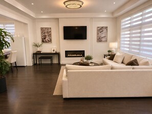 A modern living room with a sofa, a fireplace, a TV, and artwork on the walls. - Newly furnished luxury home in Oakville, entire home”. near Oakville Hospital. (Oakville)
