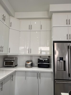 A modern kitchen with white cabinets, a stainless steel refrigerator, a toaster oven, and a coffee machine. - Newly furnished luxury home in Oakville, entire home”. near Oakville Hospital. (Oakville)