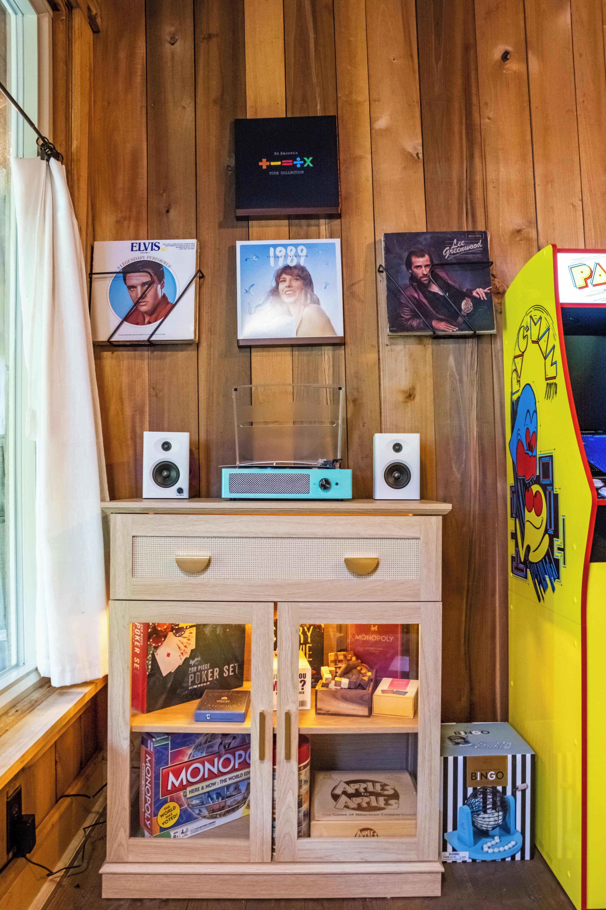 A wooden wall with framed pictures, a speaker setup, and a Monopoly game box.