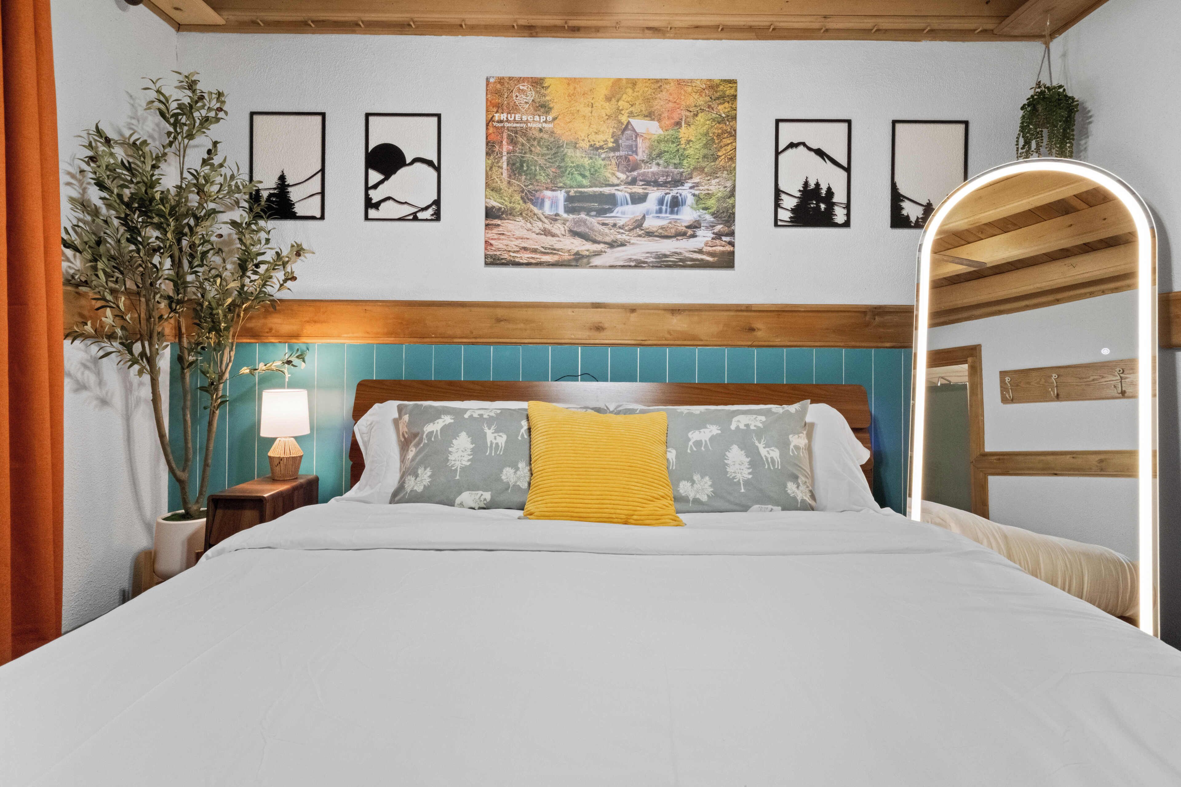 A bedroom with a bed, a nightstand, a lamp, a mirror, and framed pictures on the wall.