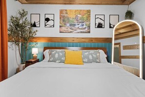 Un dormitorio con cama, mesita de noche, lámpara, espejo y cuadros en la pared.