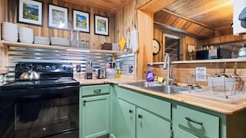 A kitchen with wooden walls, a stove, a sink, and various kitchen utensils.