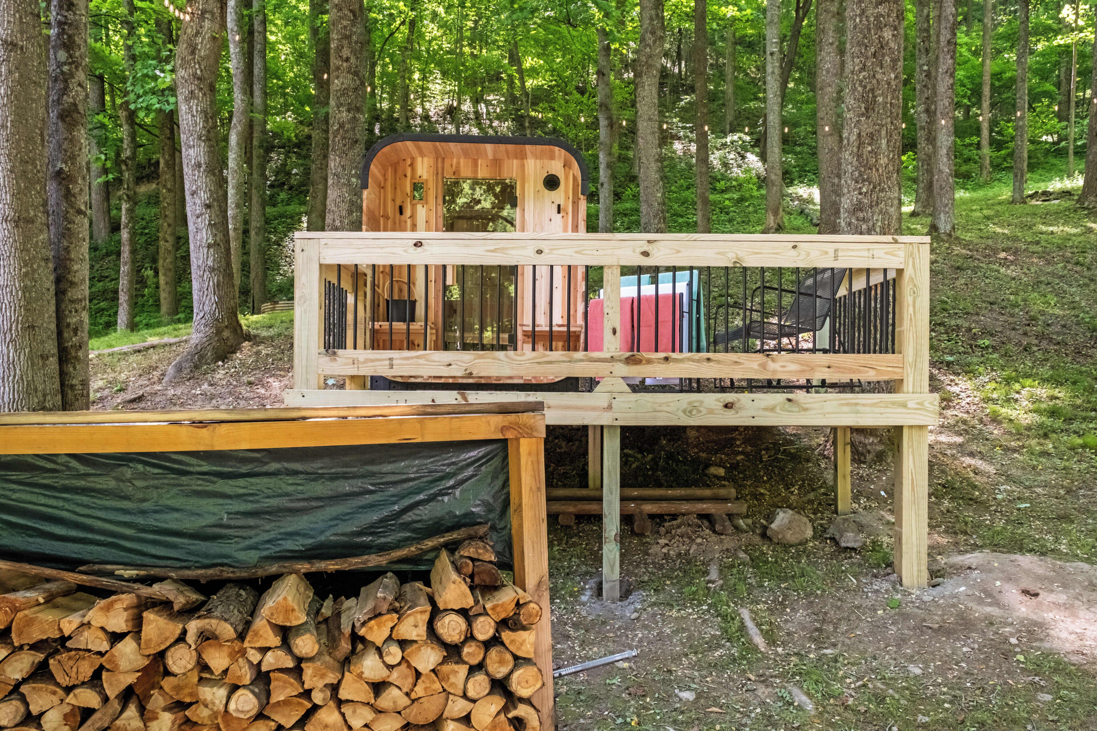A rustic wooden cabin with a deck, a pile of firewood, and a green tarp.