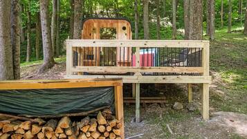 A rustic wooden cabin with a deck, a pile of firewood, and a green tarp.