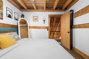 Une chambre à coucher avec un lit, des poutres en bois au plafond, une porte et un mur orné de tableaux.