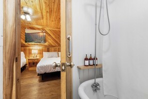 Ein Zimmer mit Holzboden, einem Bett, einem Nachttisch und einem Gemälde an der Wand.
