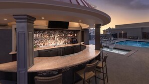 Eine Bar mit Blick auf den Pool, ausgestattet mit einer Bogenbar, Korbstühlen und einem Schwimmbecken.