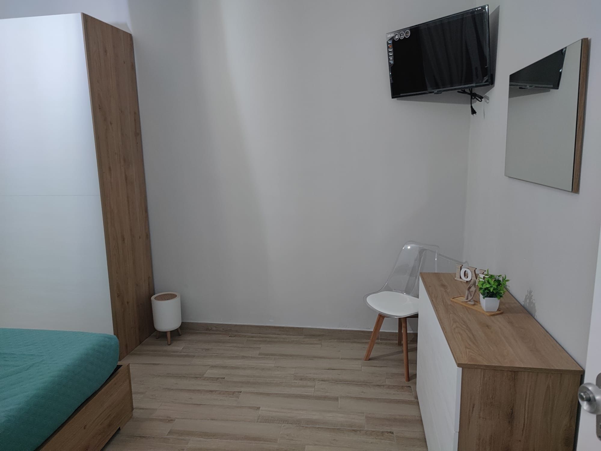 A room with a bed, a desk, a chair, a TV, and a small trash bin.