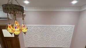A bedroom with a large bed, a decorative wall panel, a chandelier, and a bedside table with a lamp. - Nodirabegim Boutique Hotel (Bukhara)
