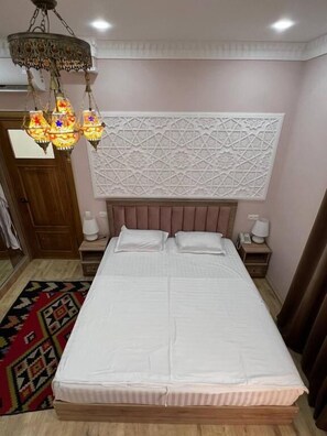 Ein Schlafzimmer mit einem großen Bett, einer dekorativen Wandverkleidung, einer Chandelierleuchtre und einem Nachttisch mit Lampe.