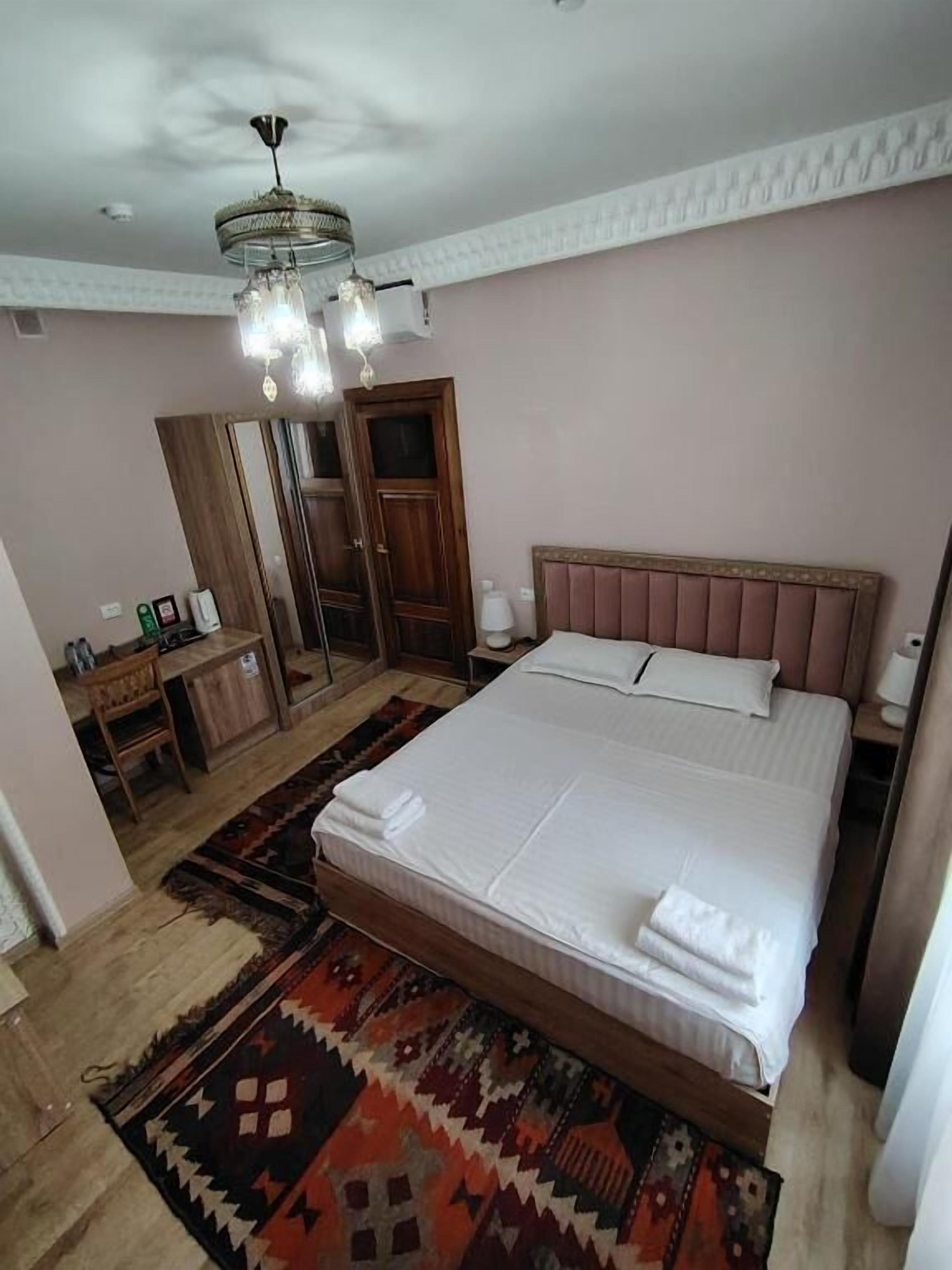 A bedroom with a large bed, a wooden headboard, a chandelier, a wardrobe, and a mirror.