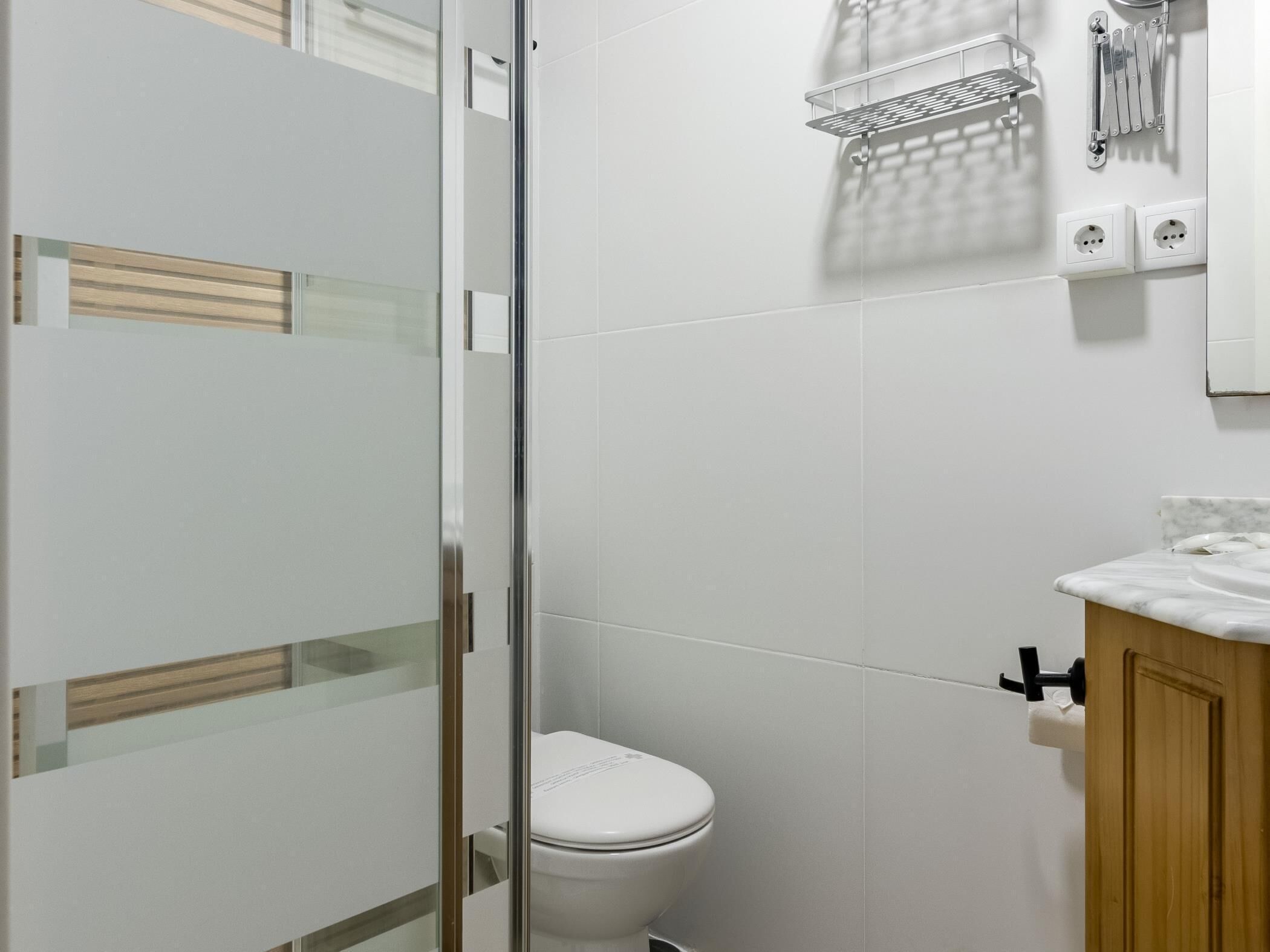 A bathroom with a glass shower enclosure, a white toilet, and a marble sink.