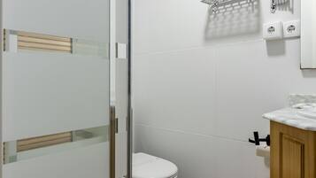A bathroom with a glass shower enclosure, a white toilet, and a marble sink.