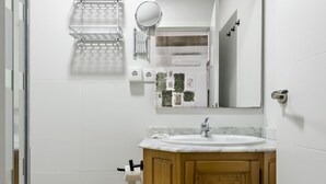 Een badkamer met een houten wastafelmeubel, een witte wasbak, een spiegel en een handdoekrek.