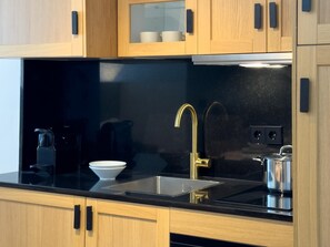 Eine moderne Küche mit Holzschränken, einer schwarzen Arbeitsplatte, einem goldenen Wasserhahn und einem Wasserkocher.