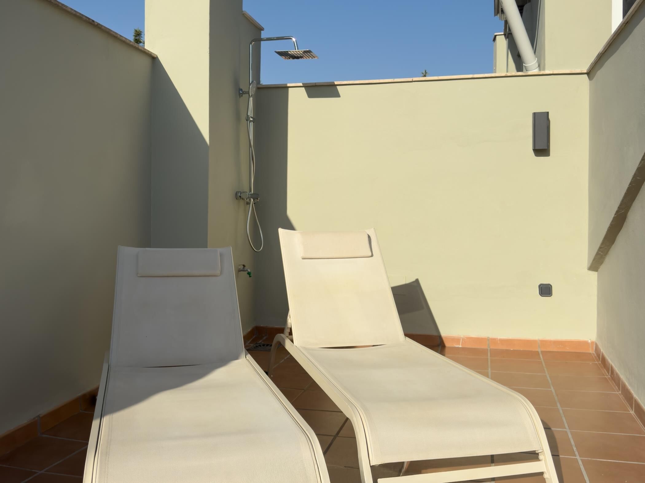 Terraza en la azotea con dos sillones blancos y una ducha integrada.