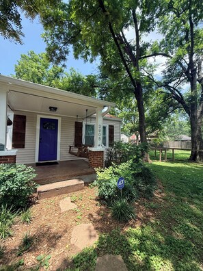 A single-story house with a blue door, a covered porch, and a brick foundation. - East Nashville Bungalow, Your New Music City Homebase MidTerm Rental DOGFRIENDLY (Nashville)