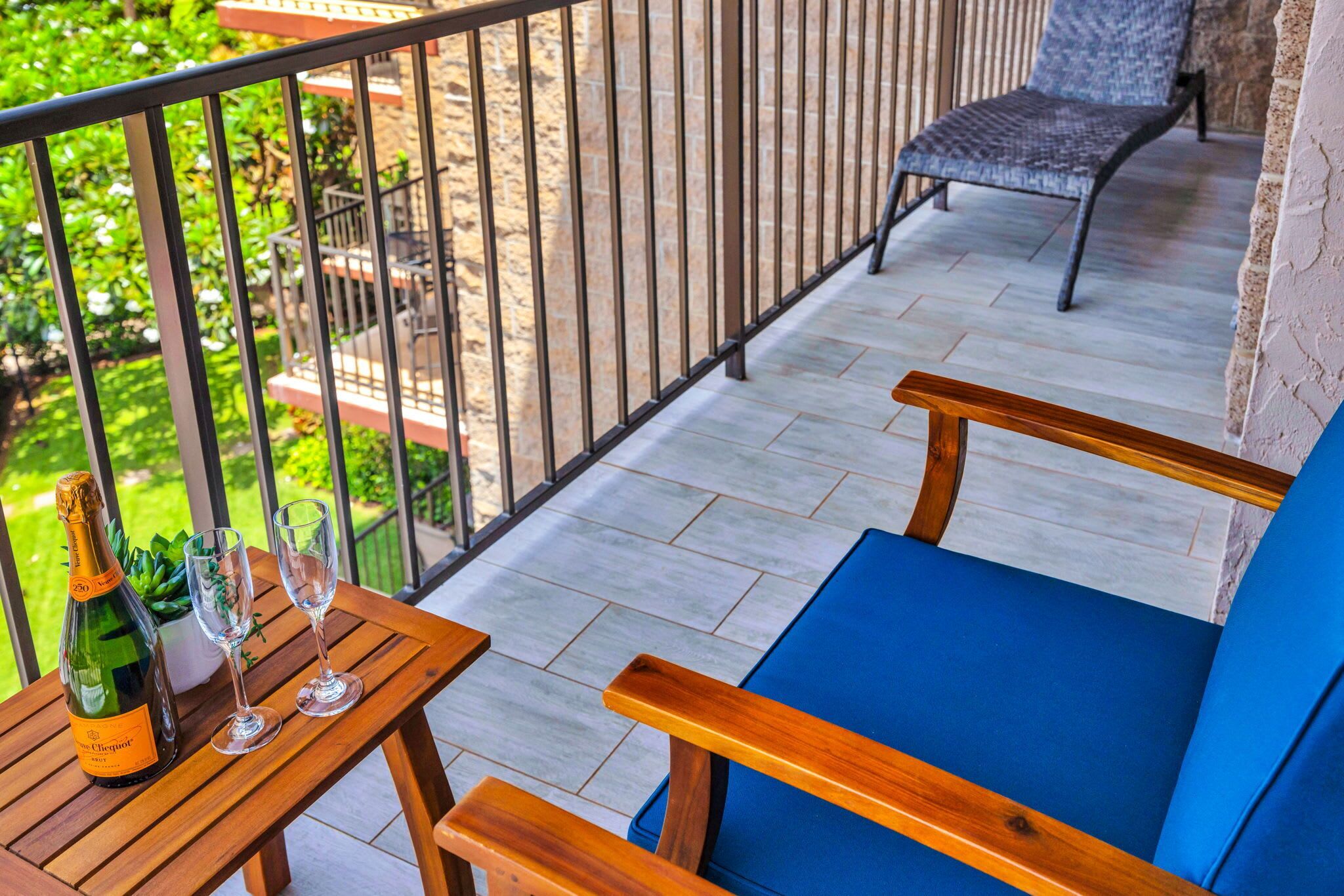 A balcony with a wooden table, two chairs, a bottle of wine, and a glass.