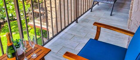 A balcony with a wooden table, two chairs, a bottle of wine, and a glass.
