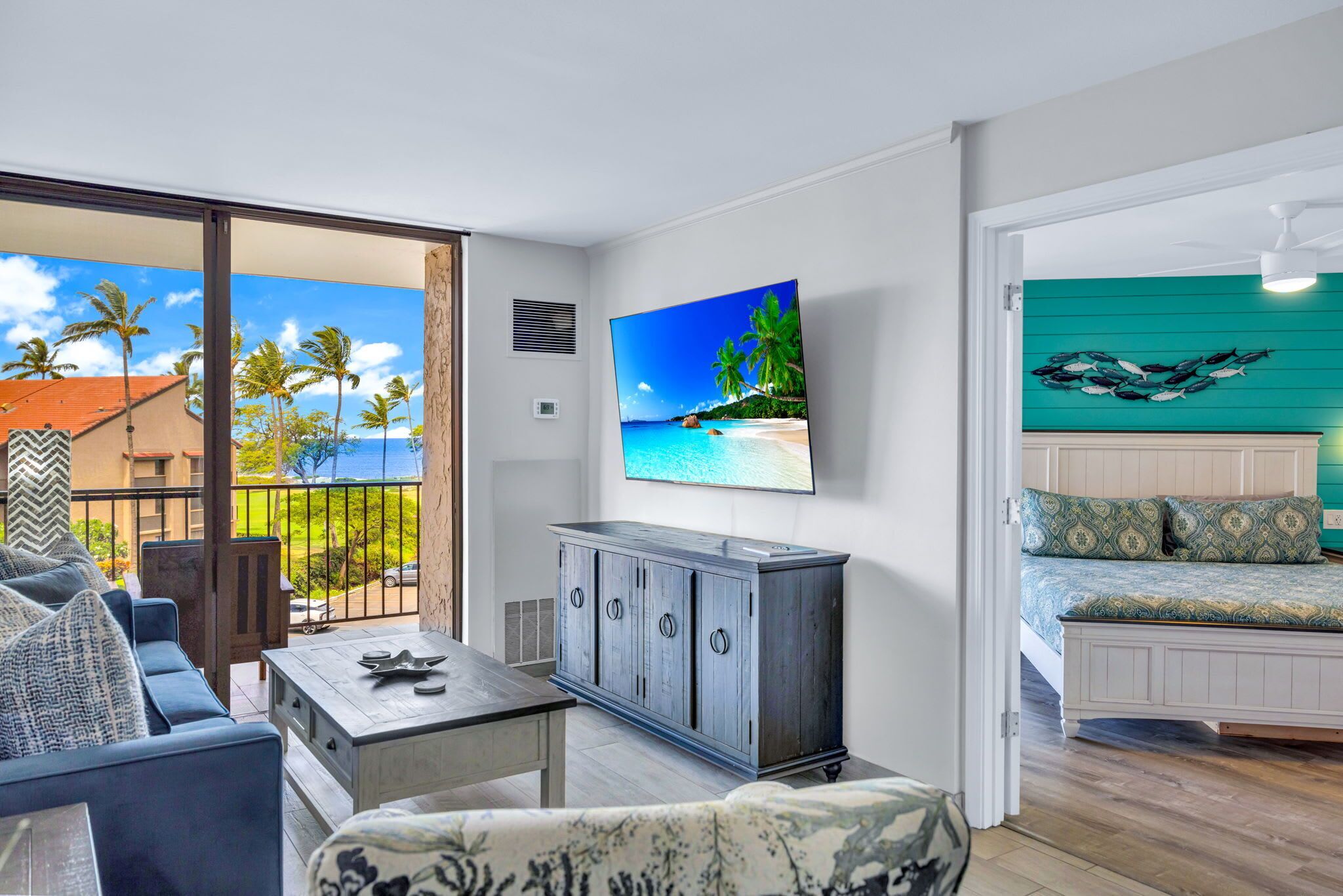 Ein Zimmer mit Balkon, einem Bett mit gemusterten Textilien, einem Schrank und einem an der Wand befestigten Fernseher.