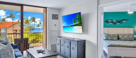 A room with a balcony, a bed with patterned bedding, a cabinet, and a wall-mounted TV.