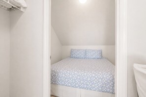 Quarto pequeno com cama de solteiro, teto inclinado e prateleira embutida.
