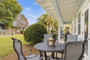 Eine Terrasse im Freien mit einem runden Tisch, Stühlen, einer Laterne und Blick auf ein Haus und Bäume.