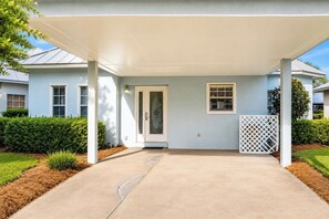 A covered entryway to a house with a concrete path leading to the door, surrounded by greenery and a white fence. - Mainsail Miramar Beach | Coastal Cottage | Sleep 9 (Miramar Beach)