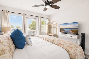 Ein Schlafzimmer mit einem Bett, einem Fernseher, einem Deckenventilator und einem Fenster mit Vorhängen.