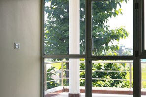 A room with a large window, a white wall, and a visible balcony railing. - President Hotel Lumbini (Lumbini)