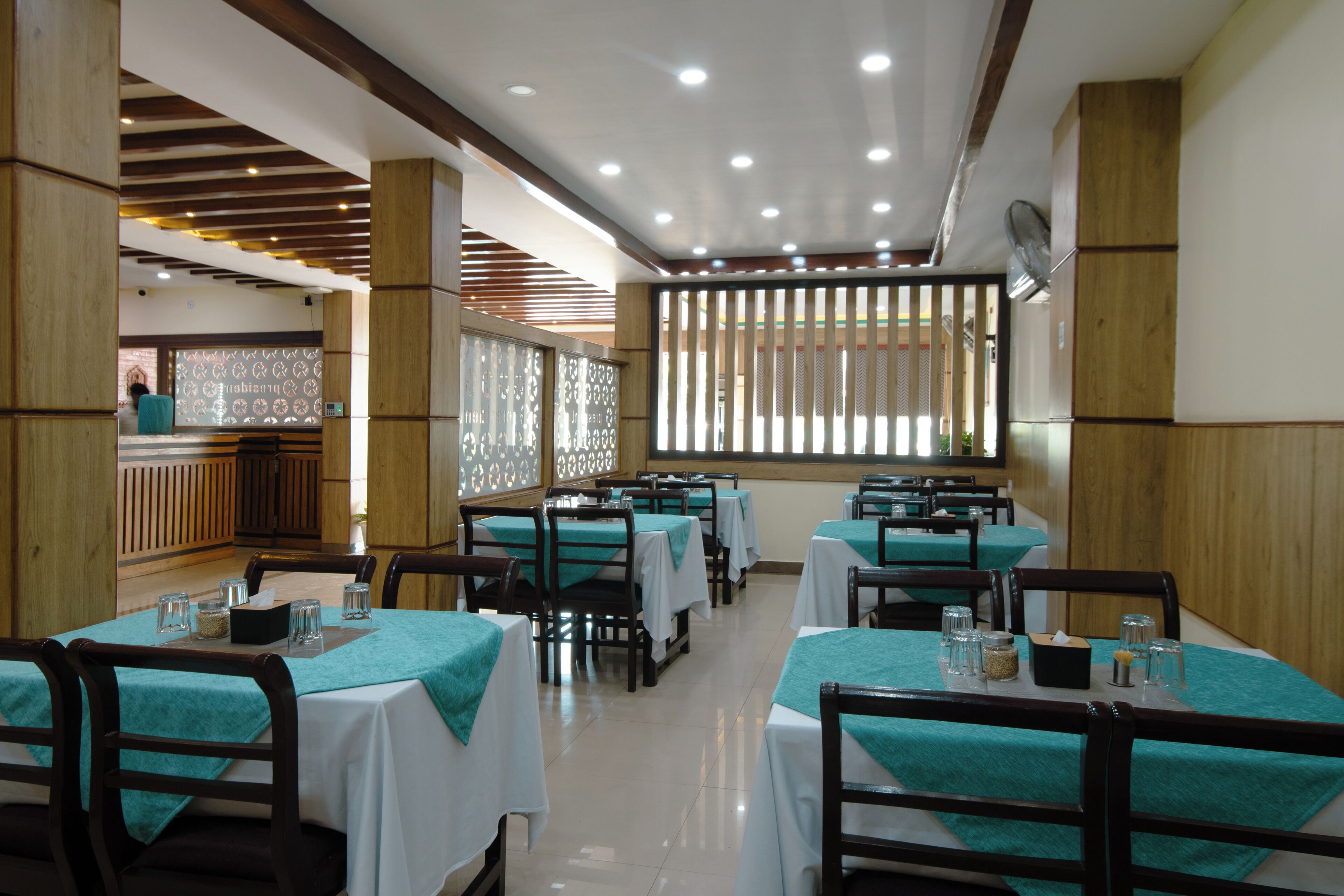 A restaurant with multiple tables, wooden pillars, and a patterned window.