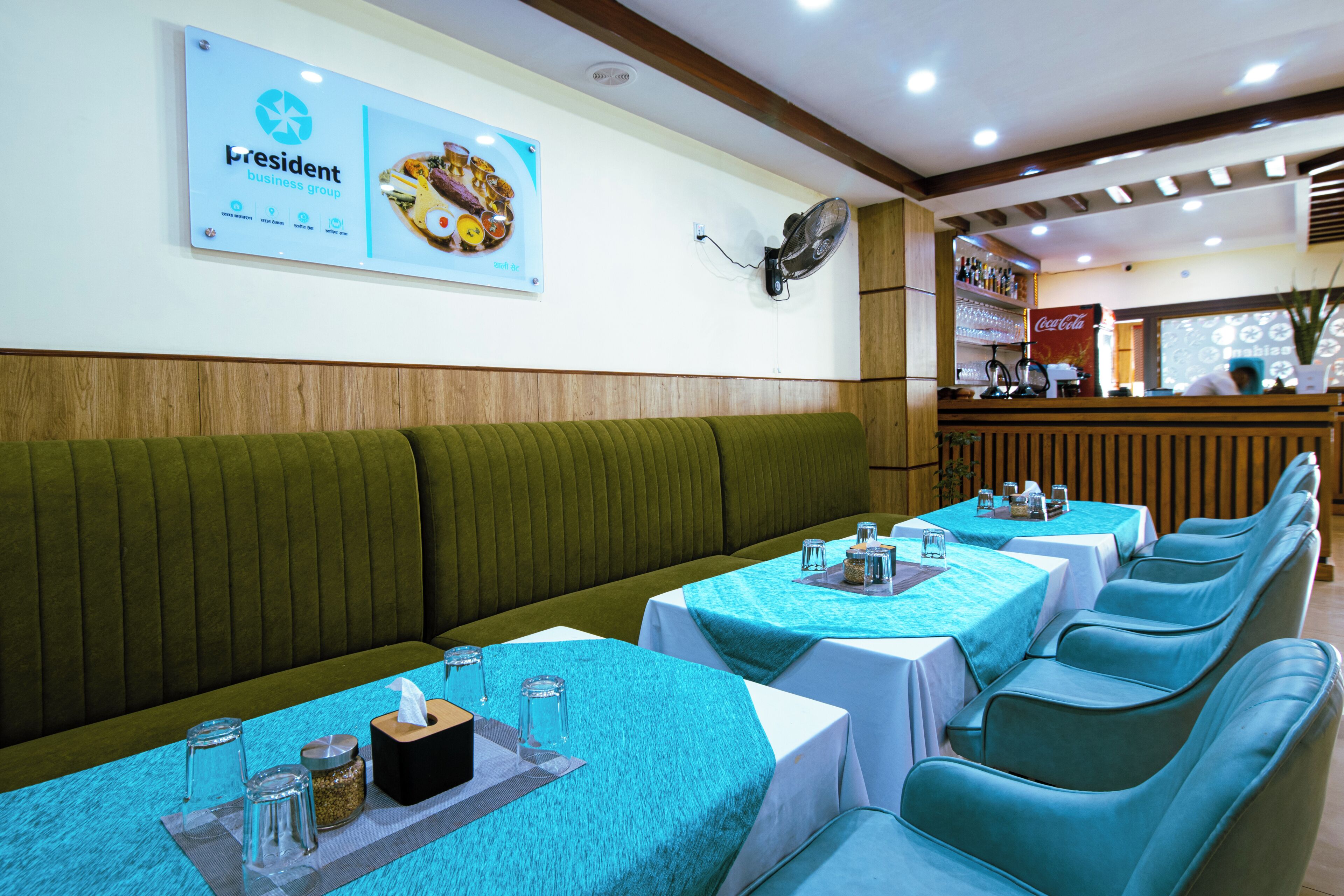 Un restaurante con cabinas verdes, mesas con manteles azules y un anuncio en la pared para el grupo empresarial President.
