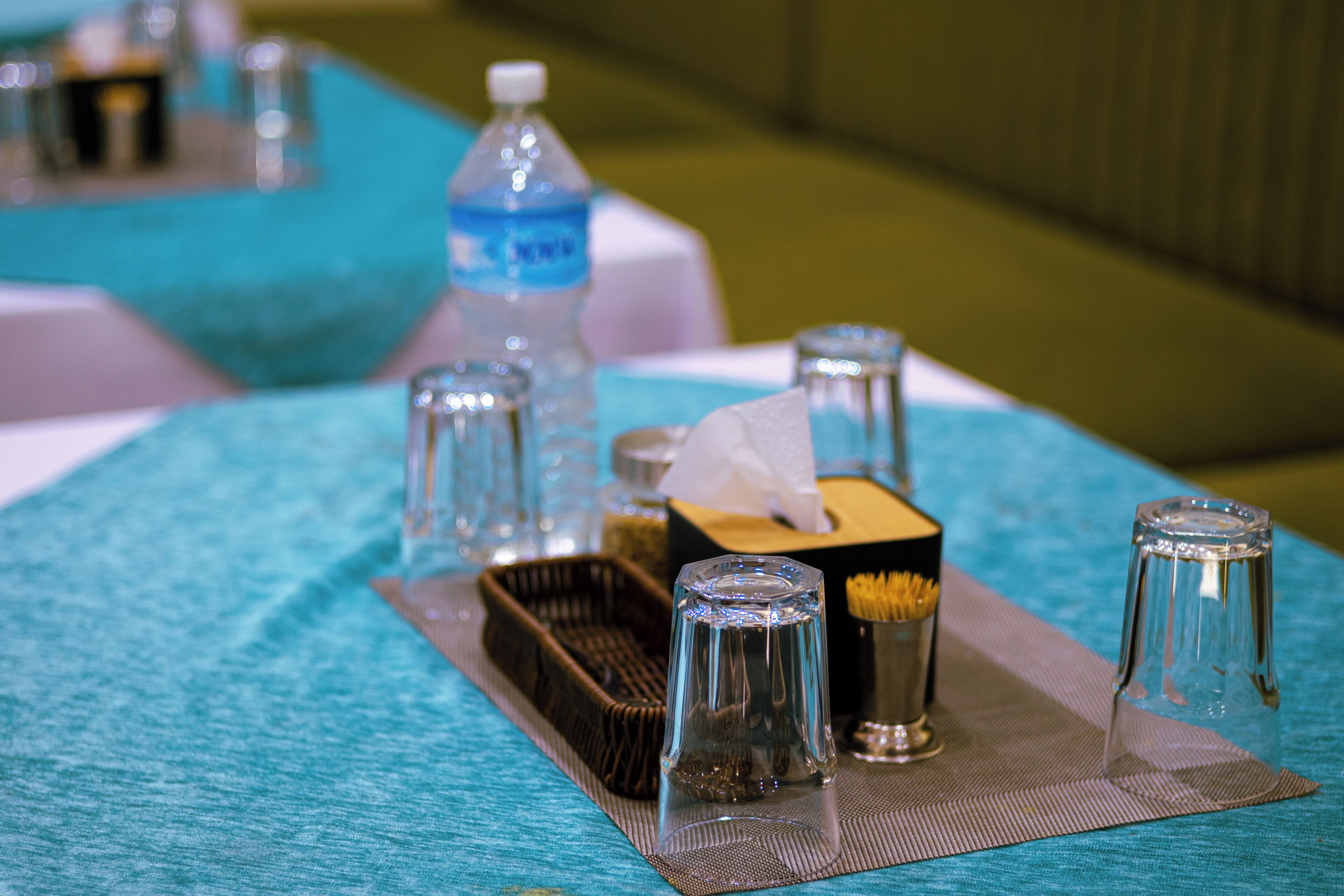 Uma mesa com uma garrafa de vidro transparente, uma caixa de lenços e vários copos.