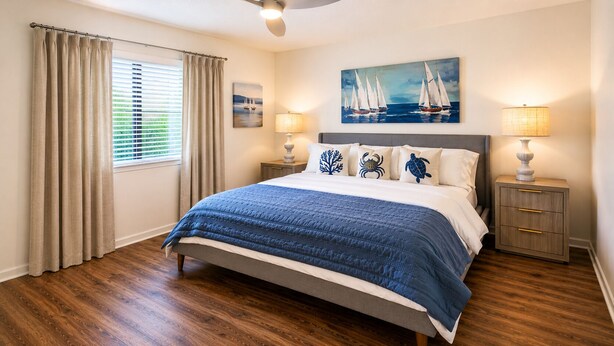 Een slaapkamer met een bed, gordijnen, een schilderij, twee nachtkastjes met lampen en een raam met zonwering.