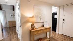 Een hal met een houten console tafel, een kunstwerk van een boom aan de muur en een welkomstbord.