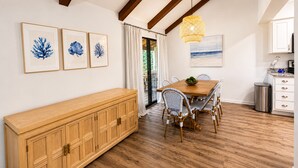 Een eethoek met een houten tafel, rieten stoelen, een buffetkast en kunstwerken in lijsten aan de muur.