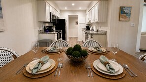 A dining room with a wooden table set for four, surrounded by white chairs. - Vita al Mare @ Seascape Resort (Miramar Beach)