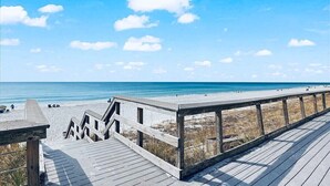 Een houten looppad naar een strand, met een heldere lucht en rustige zee.