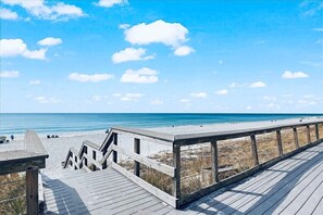 Ein hölzerner Steg führt zu einem Strand mit blauem Himmel und ruhiger See.