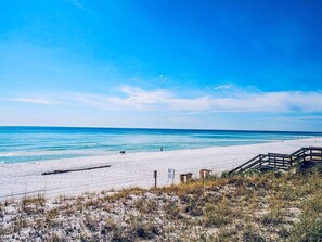 Ein Strand mit einer Holzpromenade, die zum Wasser führt, einem Sandstrand und einem klaren Himmel.