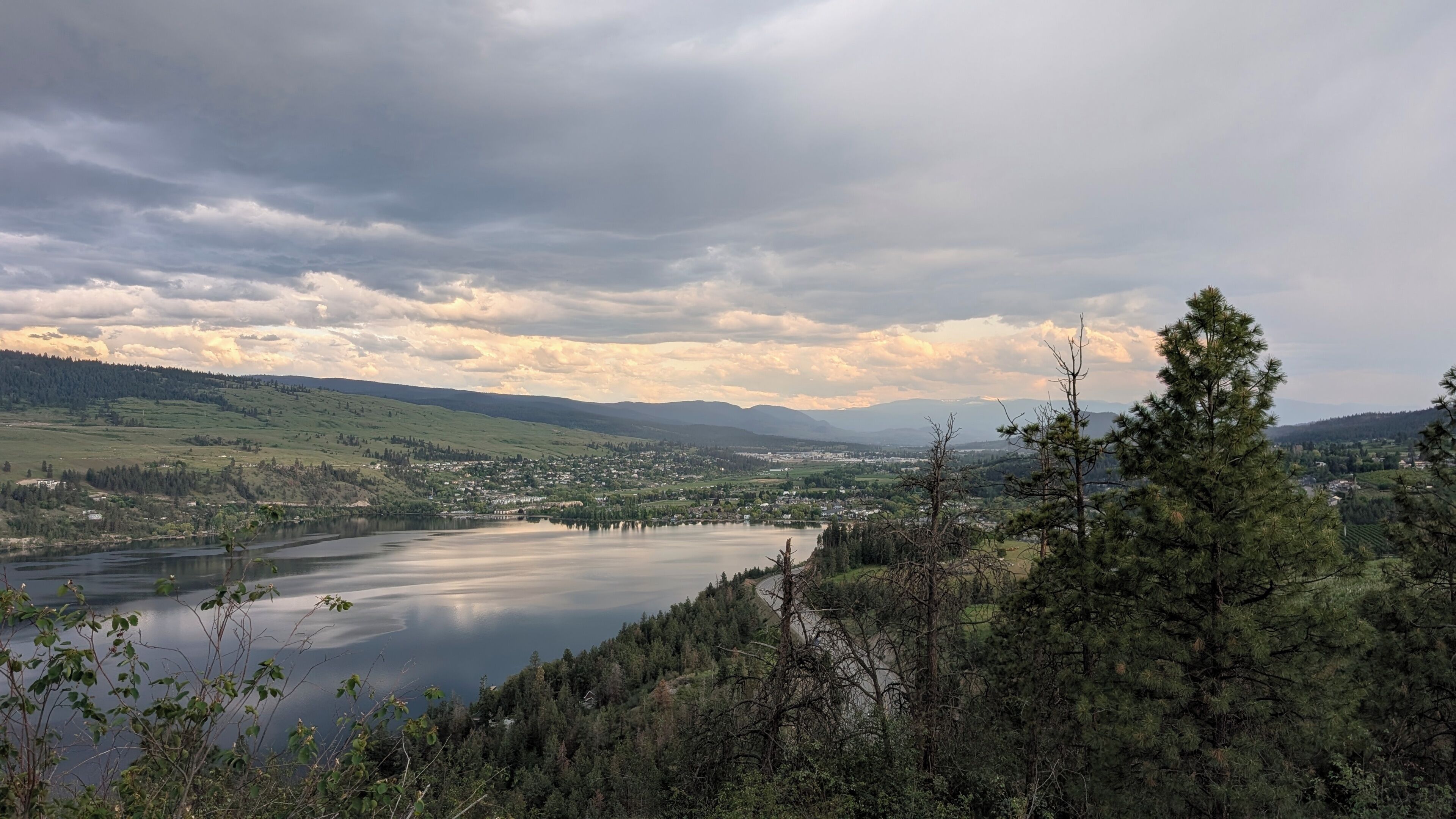Laaja panoraamanäkymä järvelle, jonka ympärillä on kukkuloita ja puita, ja kaupunki näkyy kauempana horisontissa.