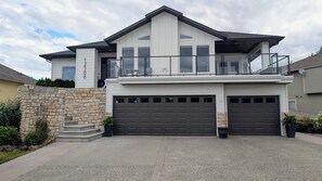 Une maison moderne à deux étages, dotée d’une façade en pierre, d’un balcon et de deux portes de garage.