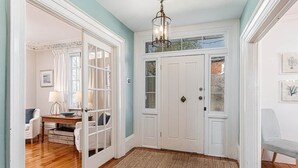 Une pièce avec un plancher en bois, une porte blanche, un lustre et un banc.