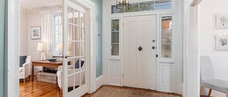 A room with a wooden floor, a white door, a chandelier, and a bench.