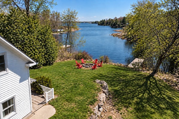 A house with a lawn, red chairs, and a view of a lake.